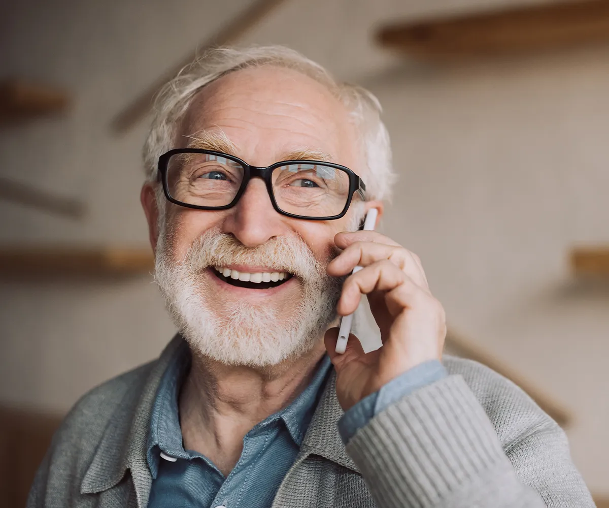 Eine älter männliche Person mit Brille auf und Handy am Ohr