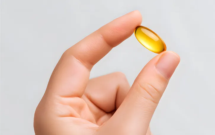 Eine gelbliche Pille zwischen Daumen und Zeigefinger einer Hand
